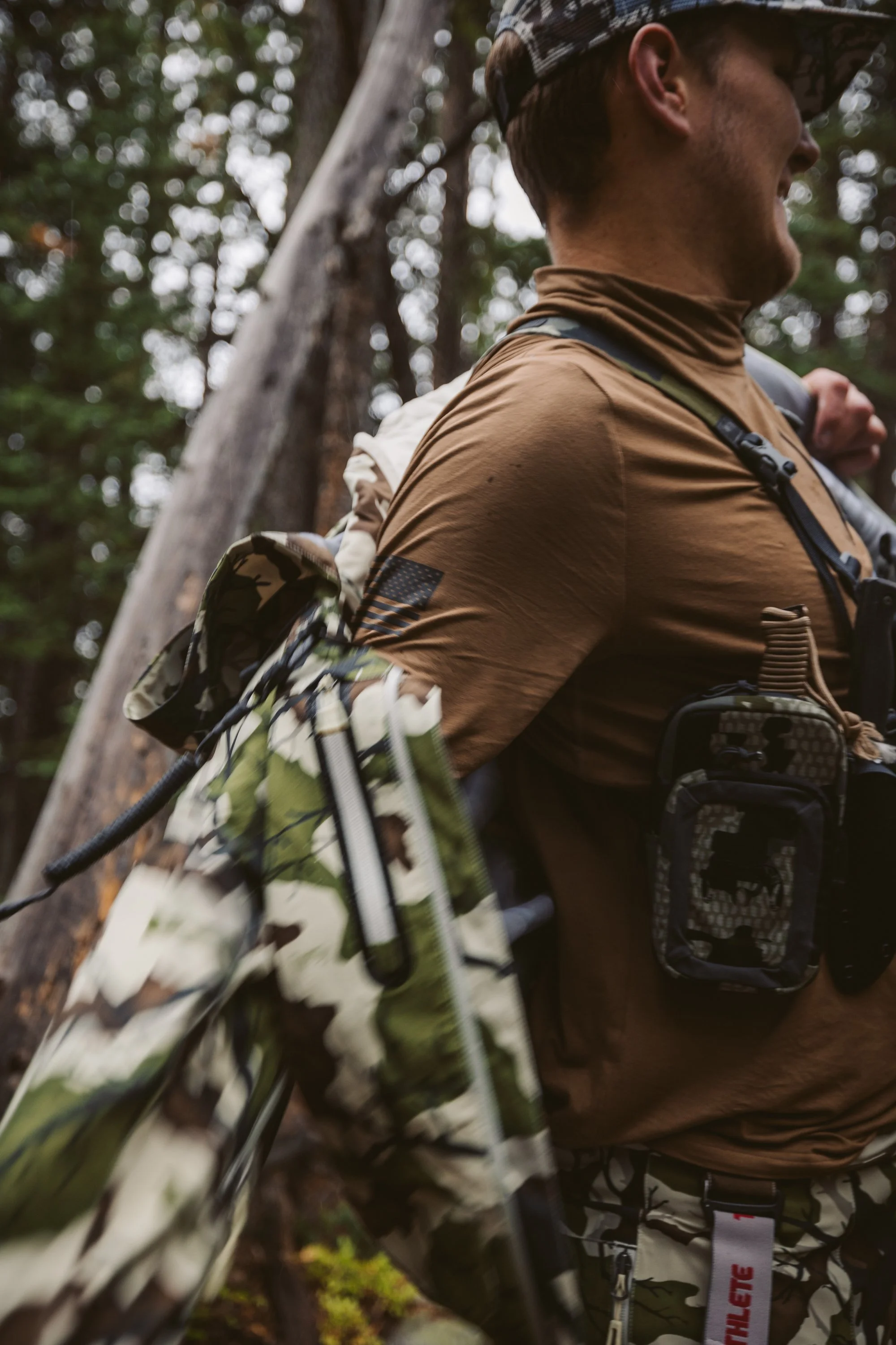 Man in brown shirt carrying camo jacket and gear in forest