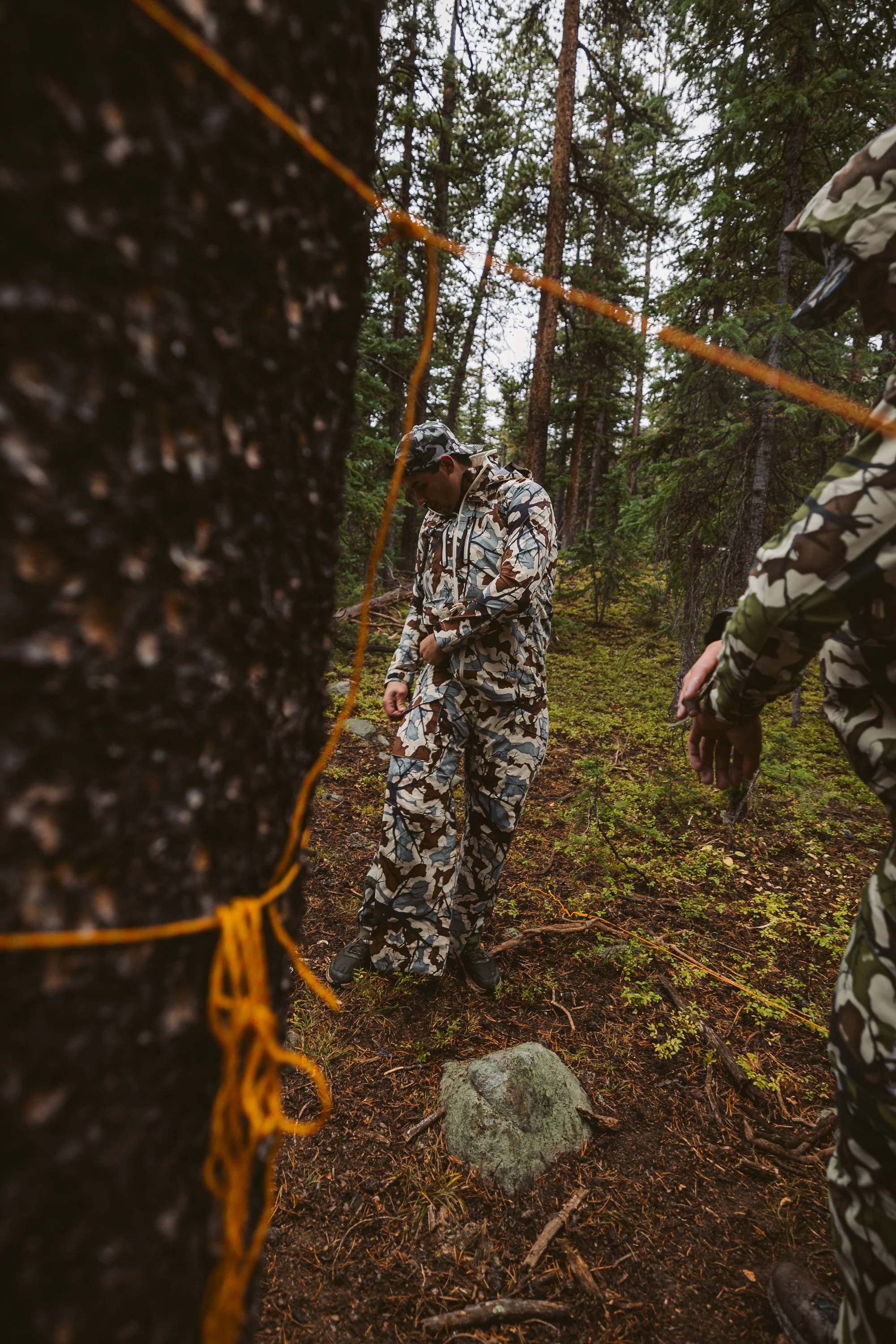 Two people in camouflage clothing setting up a survival trap in a forest.