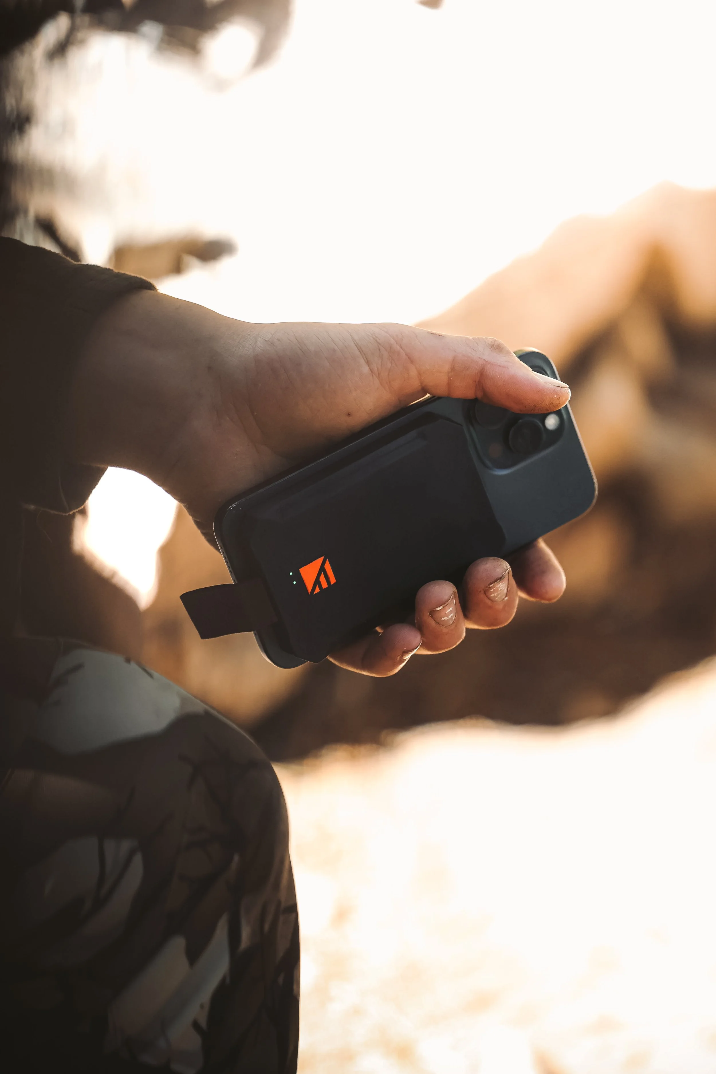 Person holding a smartphone with a rugged black case outdoors.