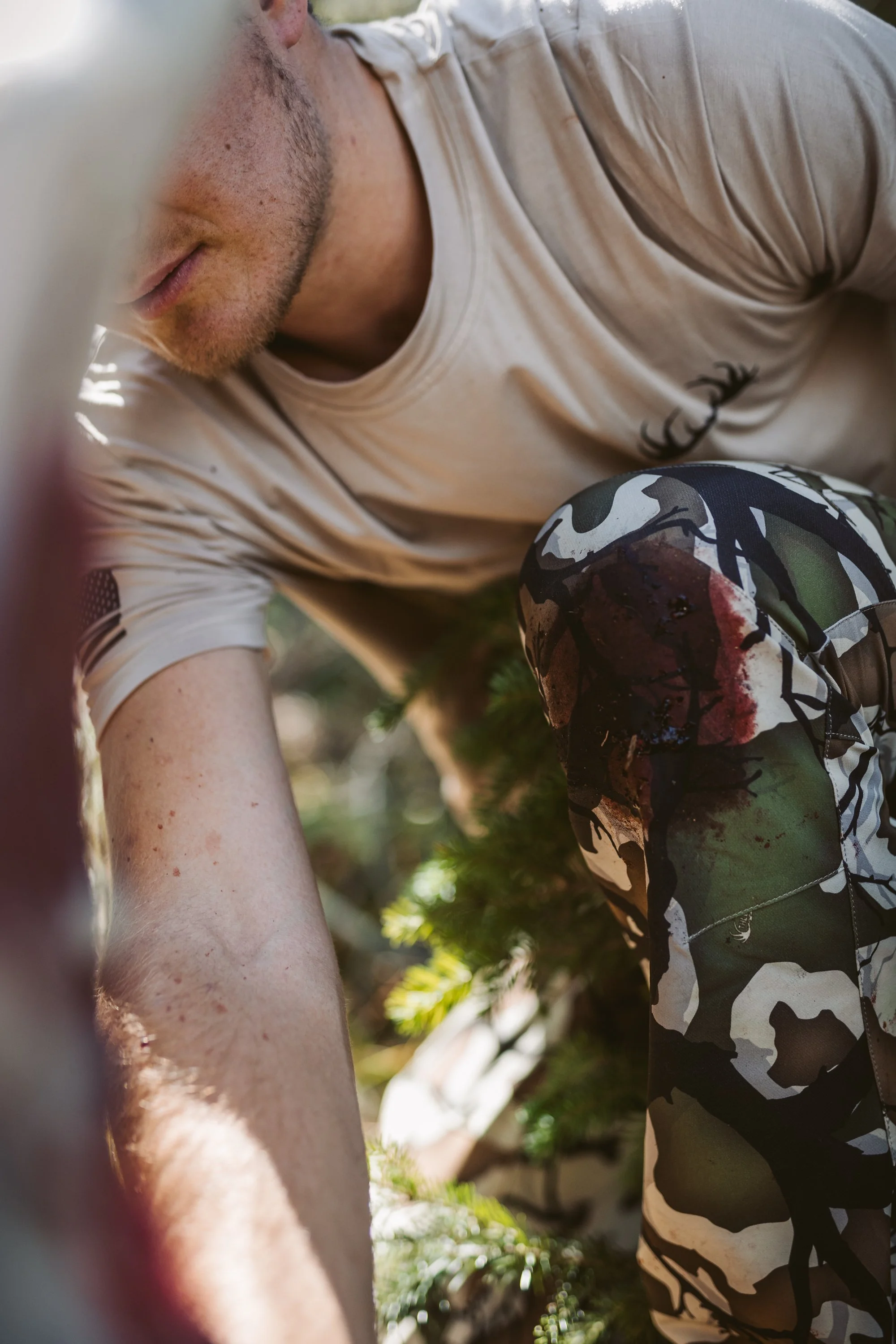 Person in camouflage pants kneeling outdoors among greenery