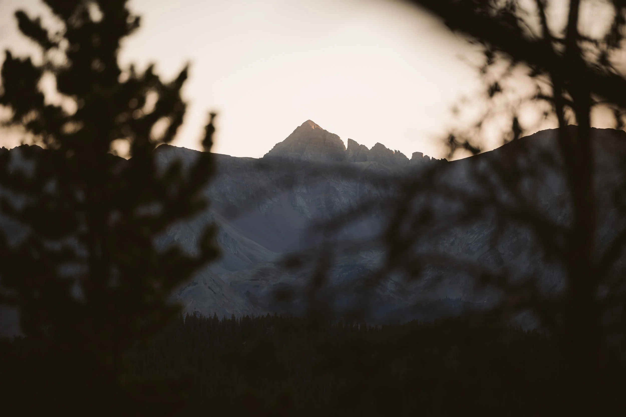 Mountain peak at sunset with silhouetted trees in the foreground.