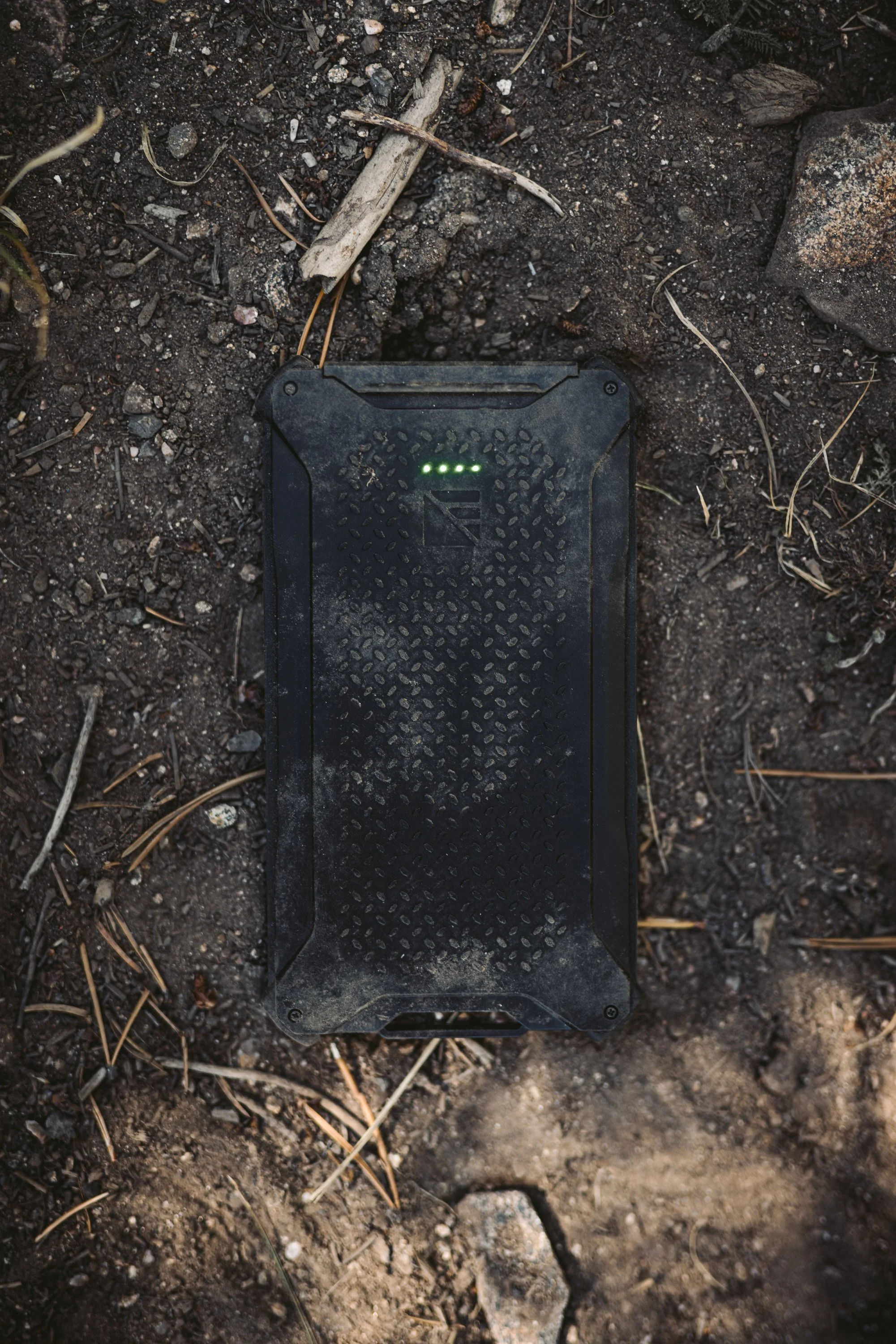 Rugged black portable power bank with LED lights on dirt surface.