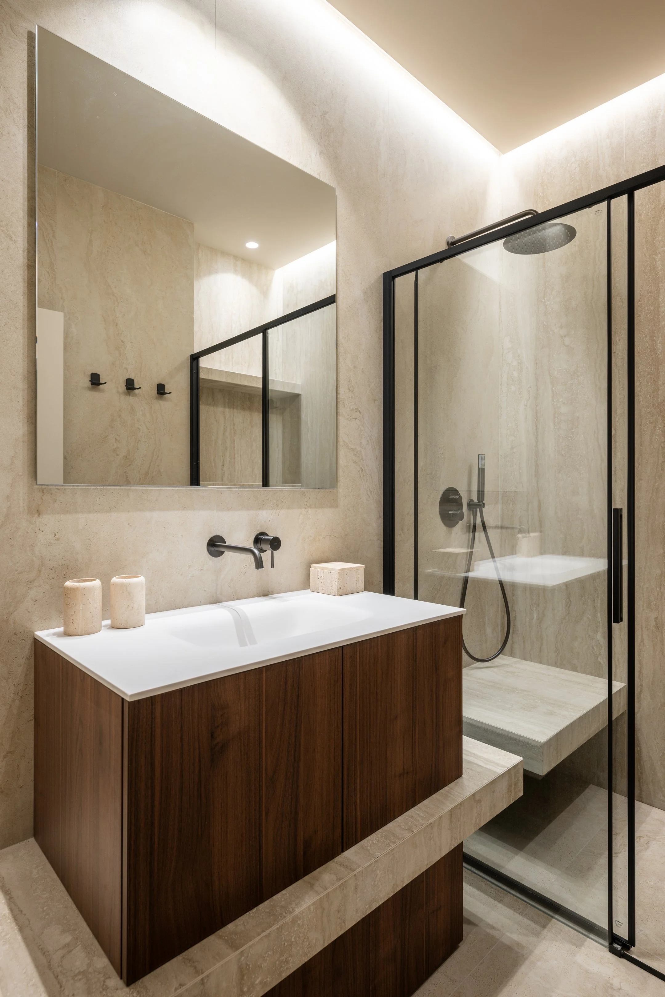 Dans un volume contraint, la salle de bain a été pensée pour offrir une expérience haut de gamme : banquette maçonnée dans la douche, continuité horizontale vasque/douche, et choix du travertin en VeinCut et CrossCut. Confort et subtilité des matière
