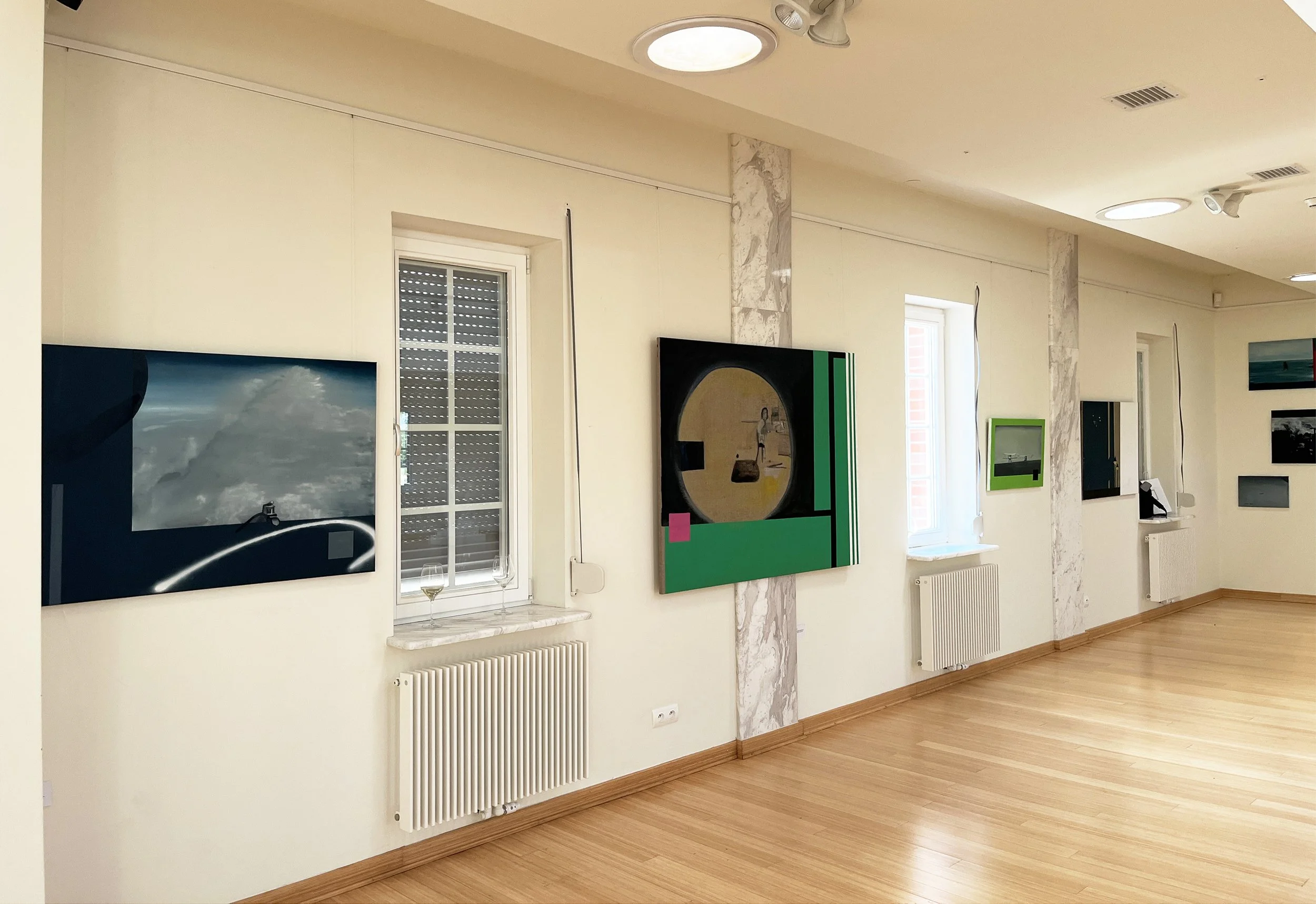 Gallery wall with framed paintings and photos, two windows, a microwave on a counter, and a radiator on the wall.