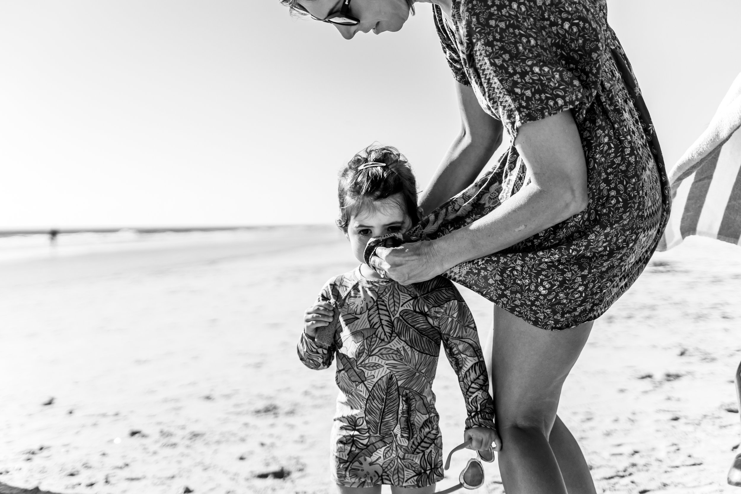 Mom blowing her daughter's nose in her dress at the beach.