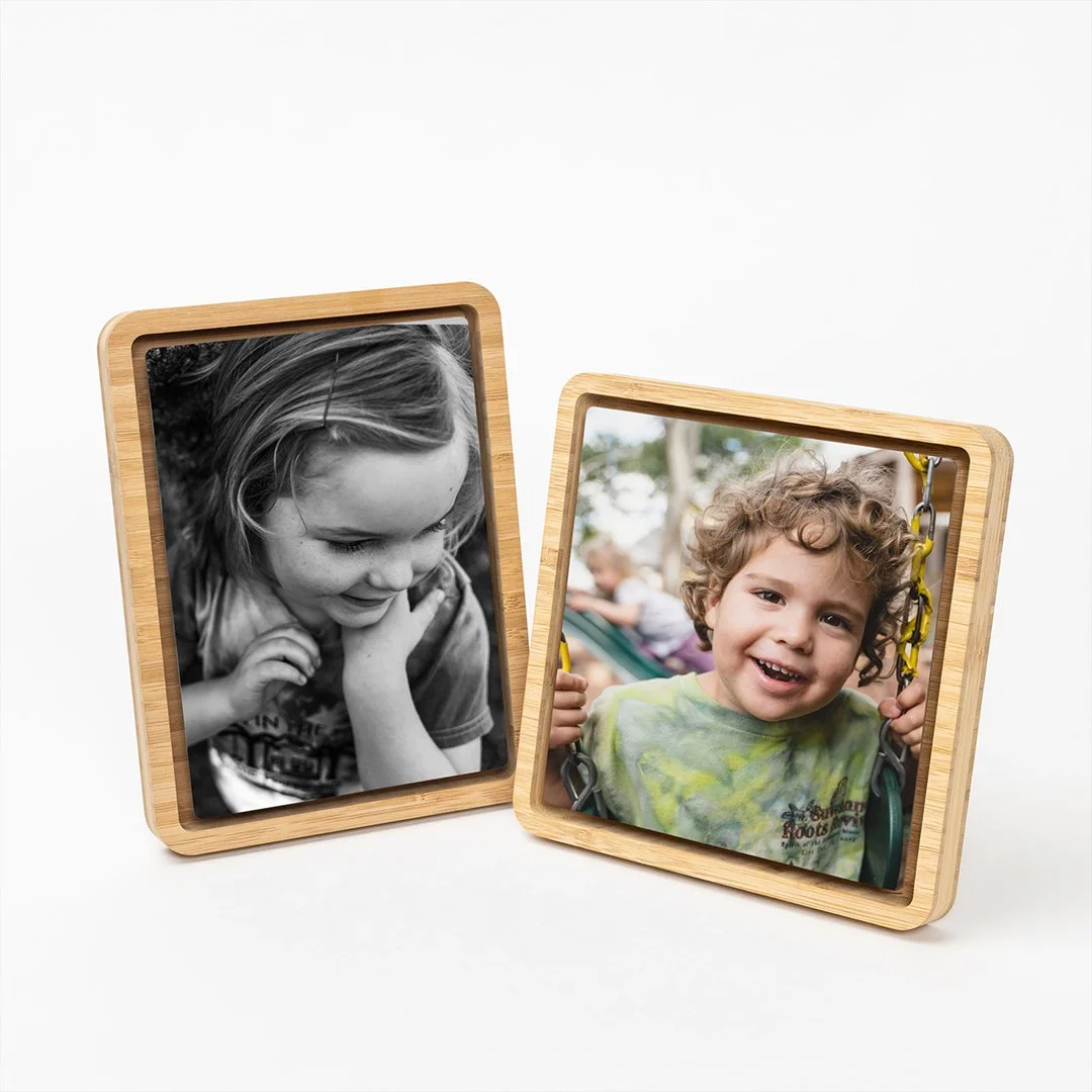 A gray photo album open to show two pages with photographs, one black and white and one color, featuring a young girl outdoors near a wooden fence and greenery.