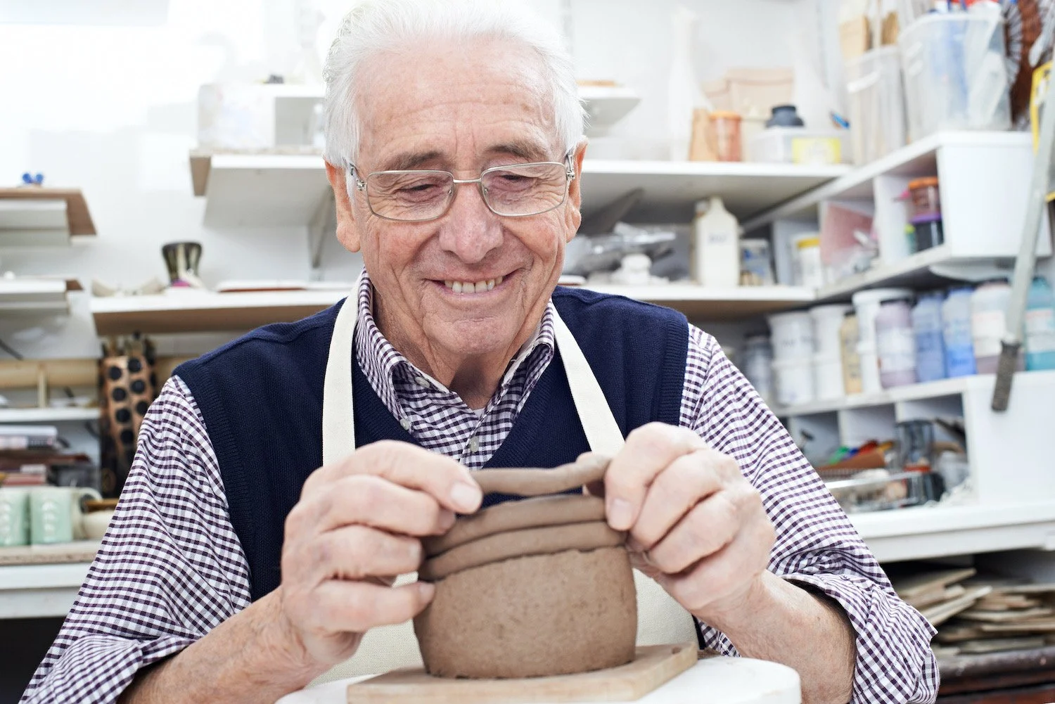 An elderly man carving a pottery bowl in a ceramics workshop.