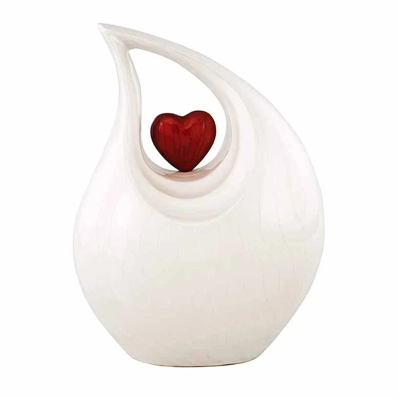Cremation urn for human ashes shaped like a white tear drop with a small red heart accent
