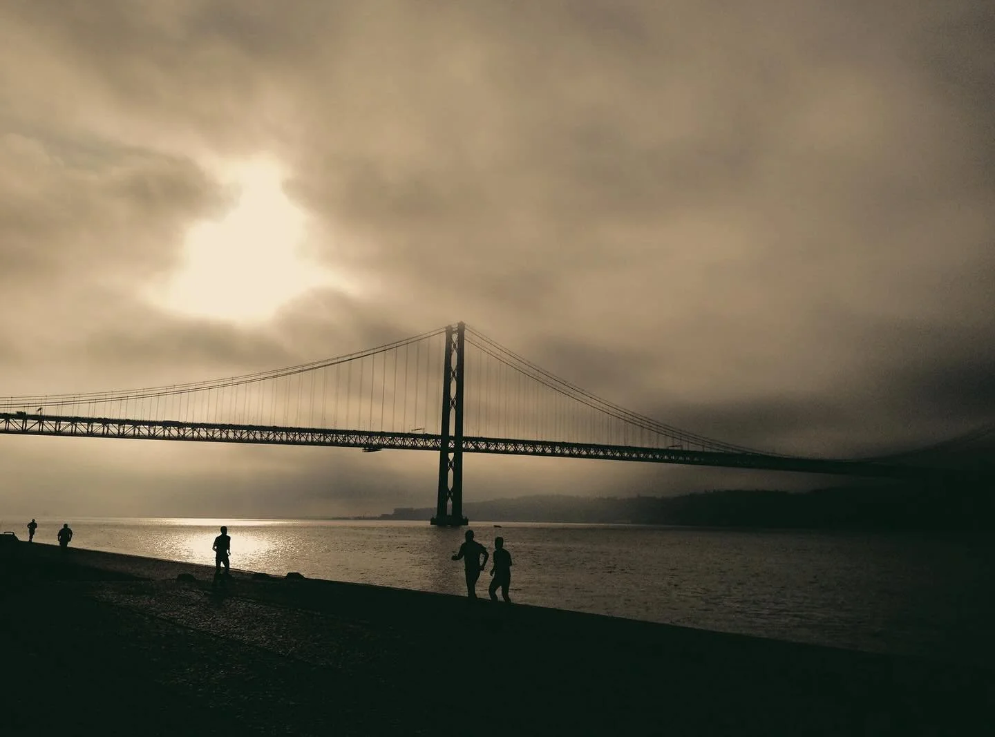 Early mornings in Bel&eacute;m carry a quiet kind of clarity.
This frame was taken along the waterfront, where the light moves slowly across the Tagus and the city feels almost paused.
The bridge&mdash;Ponte 25 de Abril&mdash;often draws comparisons 
