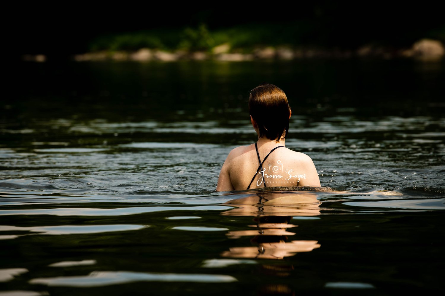 a girl swims in the Delaware River. Half of her body is above water, and the photo shows her from the back