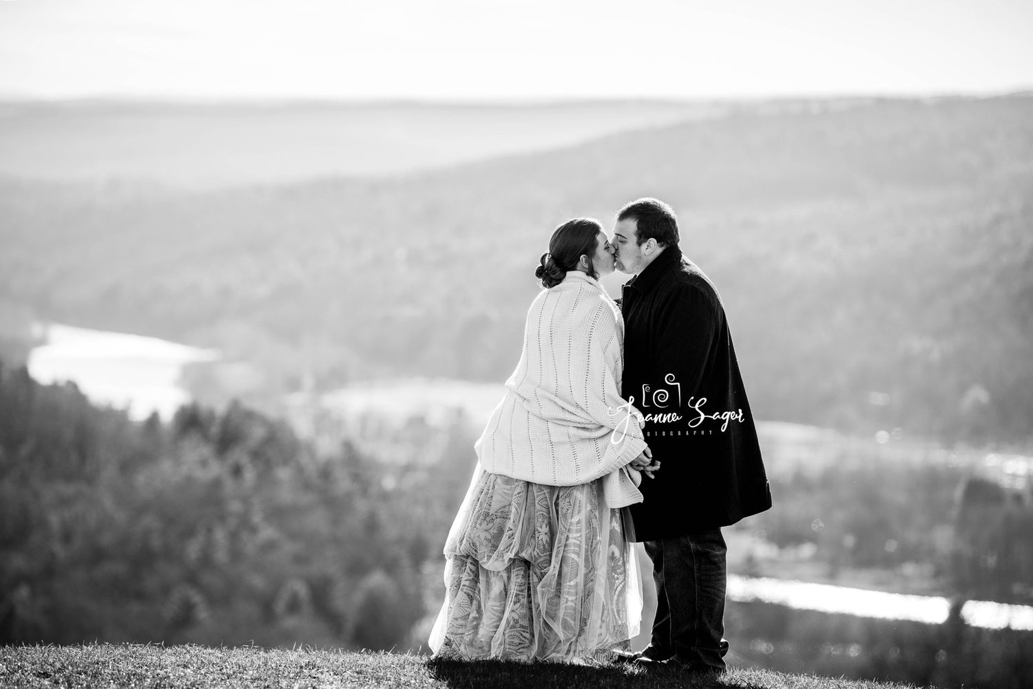 bride and groom kiss on a mountaintop with the river valley in the background behind them. the photo is in black and white