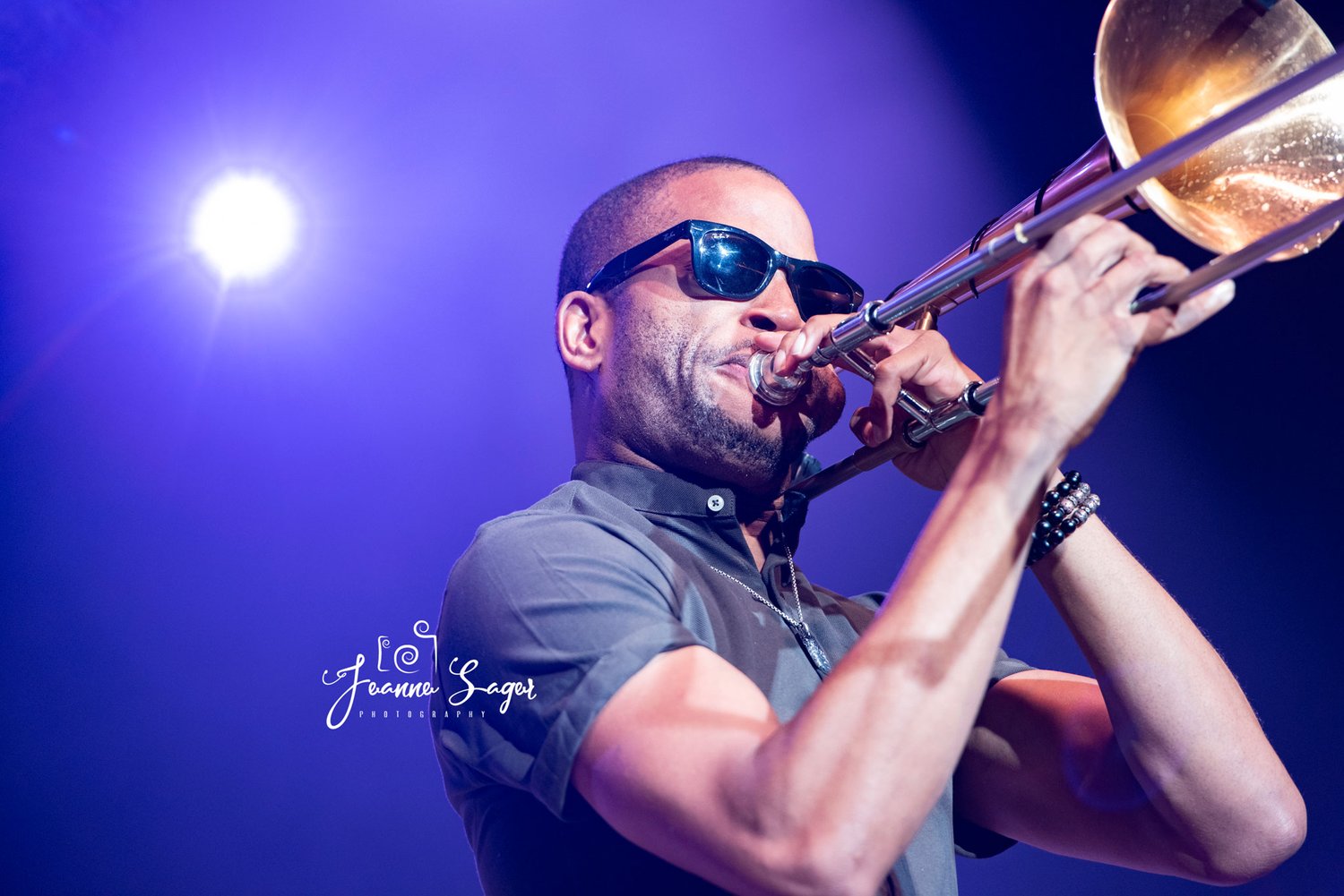 jazz musician Trombone Shorty plays a trombone in front of a purple backdrop