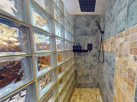 Shower area with glass block wall, gray tiled walls, and a rainfall showerhead.