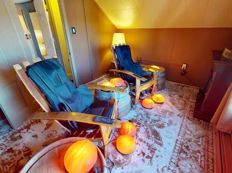 Two blue reclining chairs with small pumpkins on a side table and on the floor in a cozy, warmly lit room.
