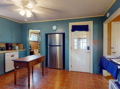 Kitchen with blue walls, wooden table, stainless steel refrigerator, white door with glass window, and a ceiling fan.