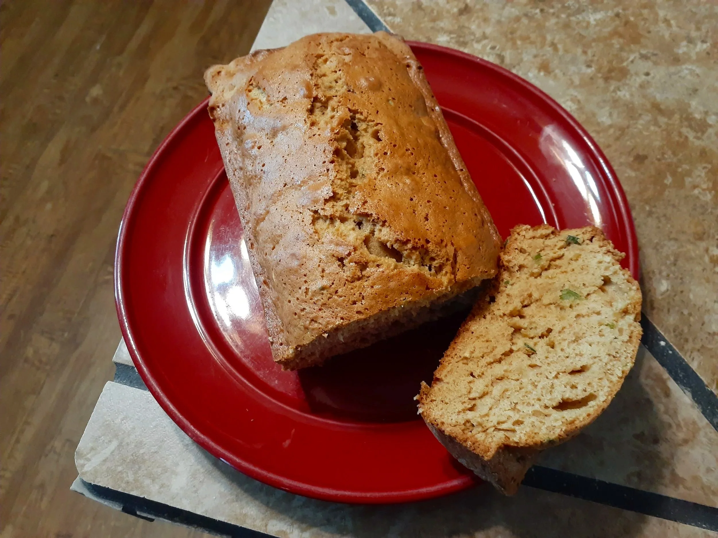 Loaf of zuchinni bread with a slice cut and placed on a red plate on a tiled table.