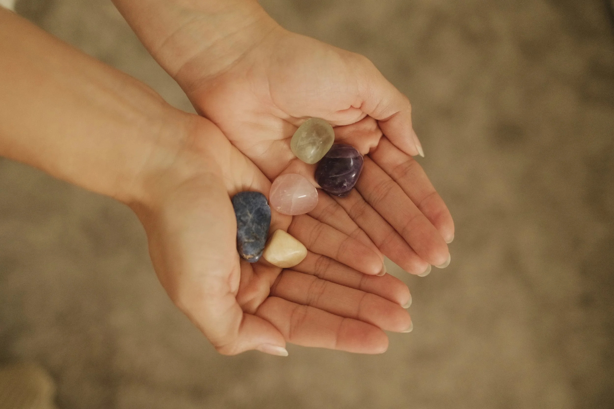 A person's hands holding several polished semi-precious gemstone stones of various colors.