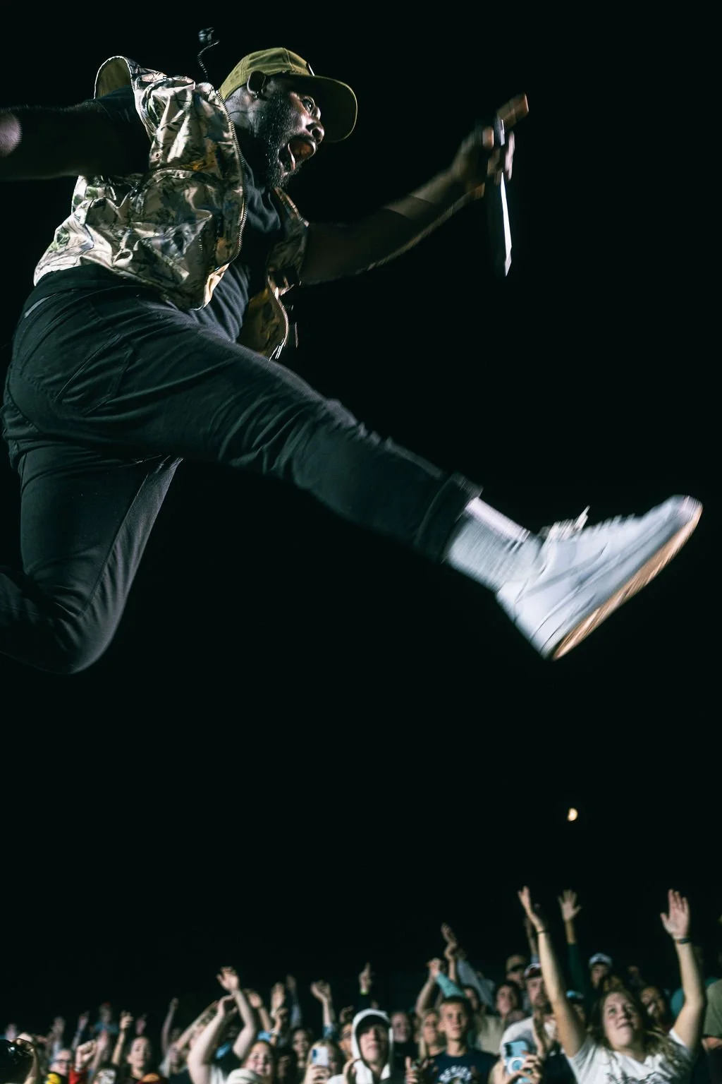 A performer jumping with a microphone in his hand in front of a crowd at night.