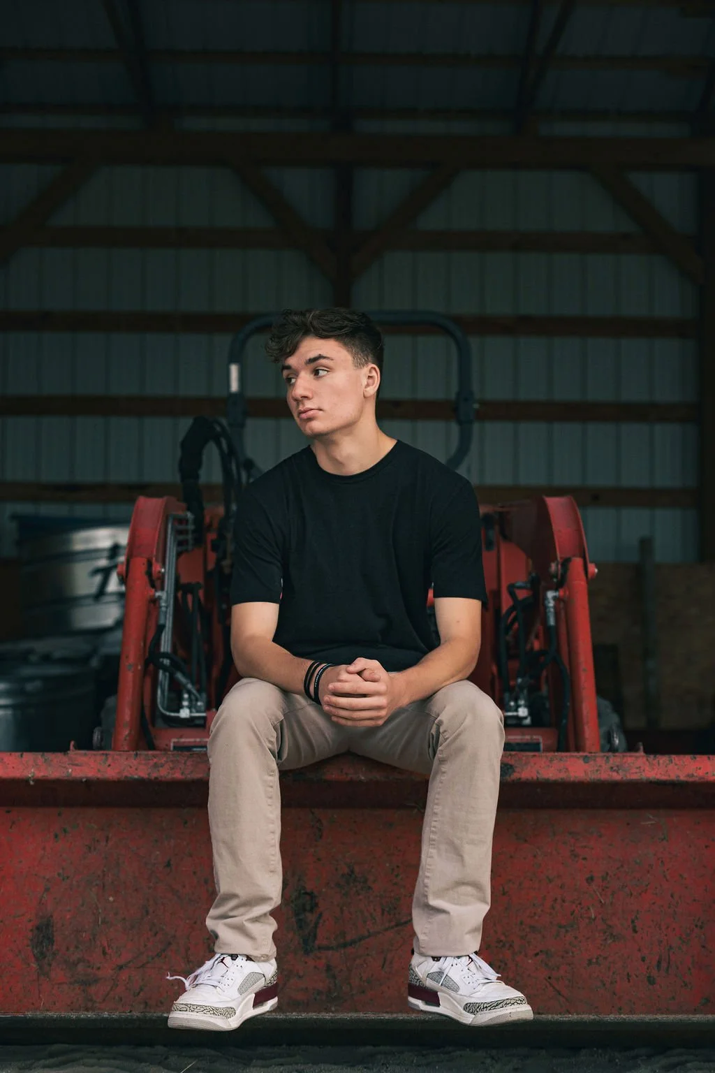Young man sitting on a red tractor inside a barn with metal walls and wooden beams