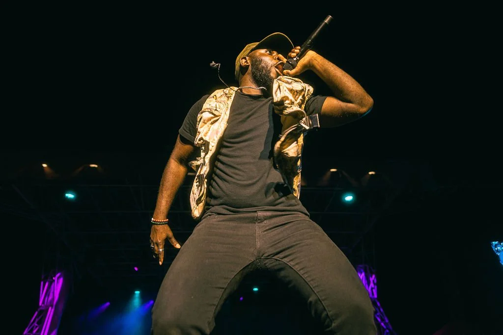 Performer singing into microphone on stage at night with colorful stage lights.