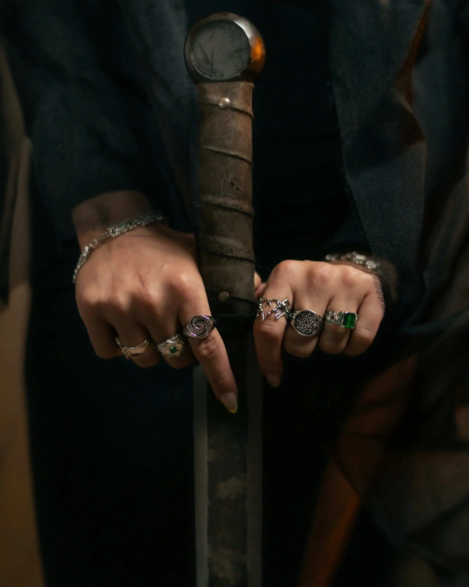 Close-up of someone holding an old, rusty knife with a wrapped handle and rings on their fingers.