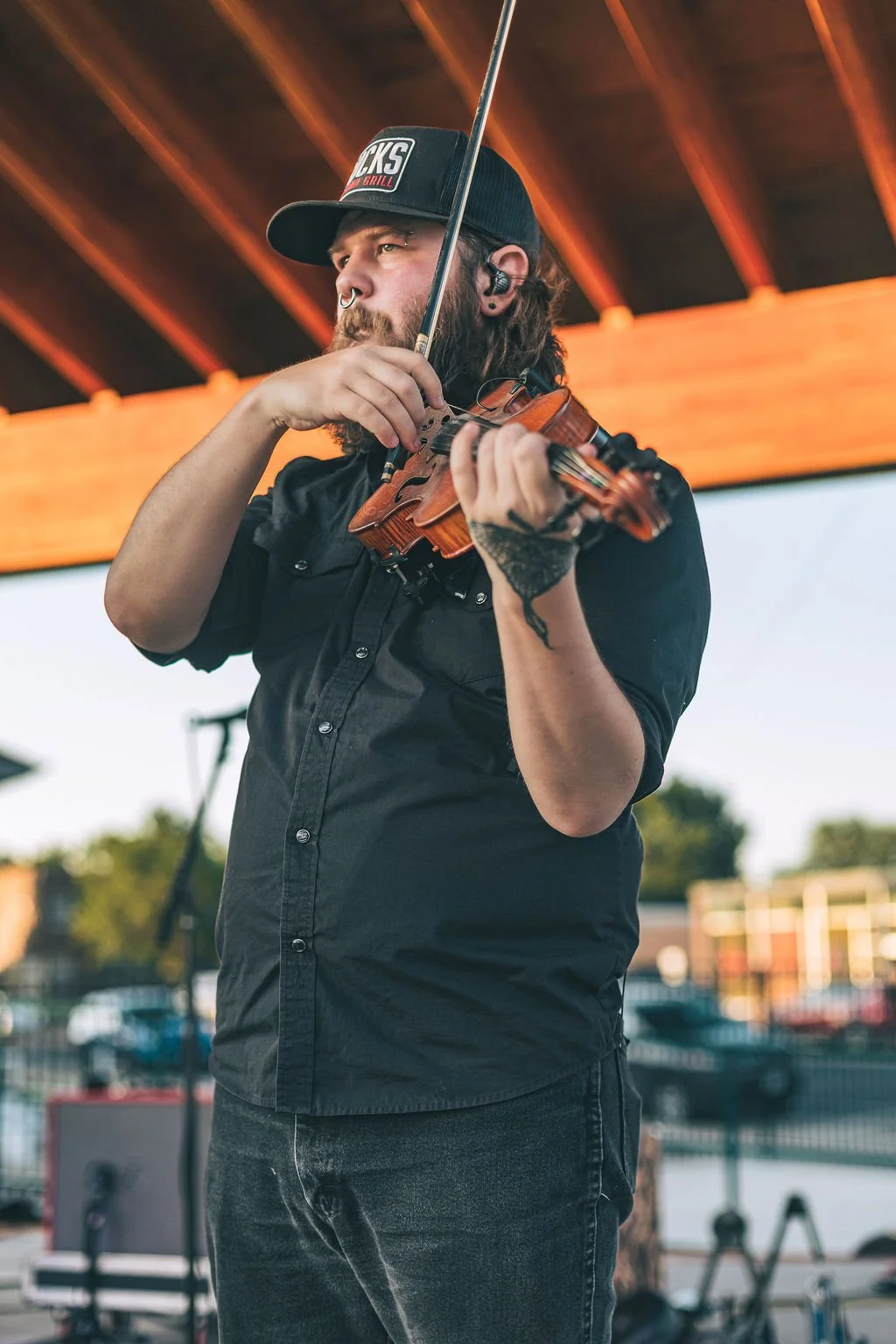 A man with a beard and long hair playing a violin outdoors during daylight.