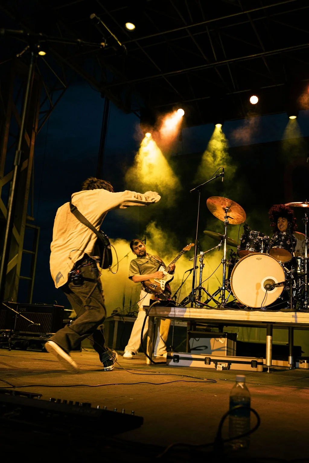 Musicians performing at an outdoor concert stage at night, with colorful spotlights illuminating the scene.