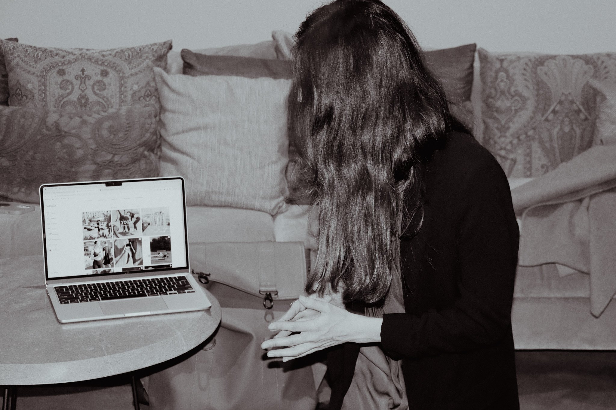 Person seated at table with open laptop, in front of decorative pillows, viewed from the side.