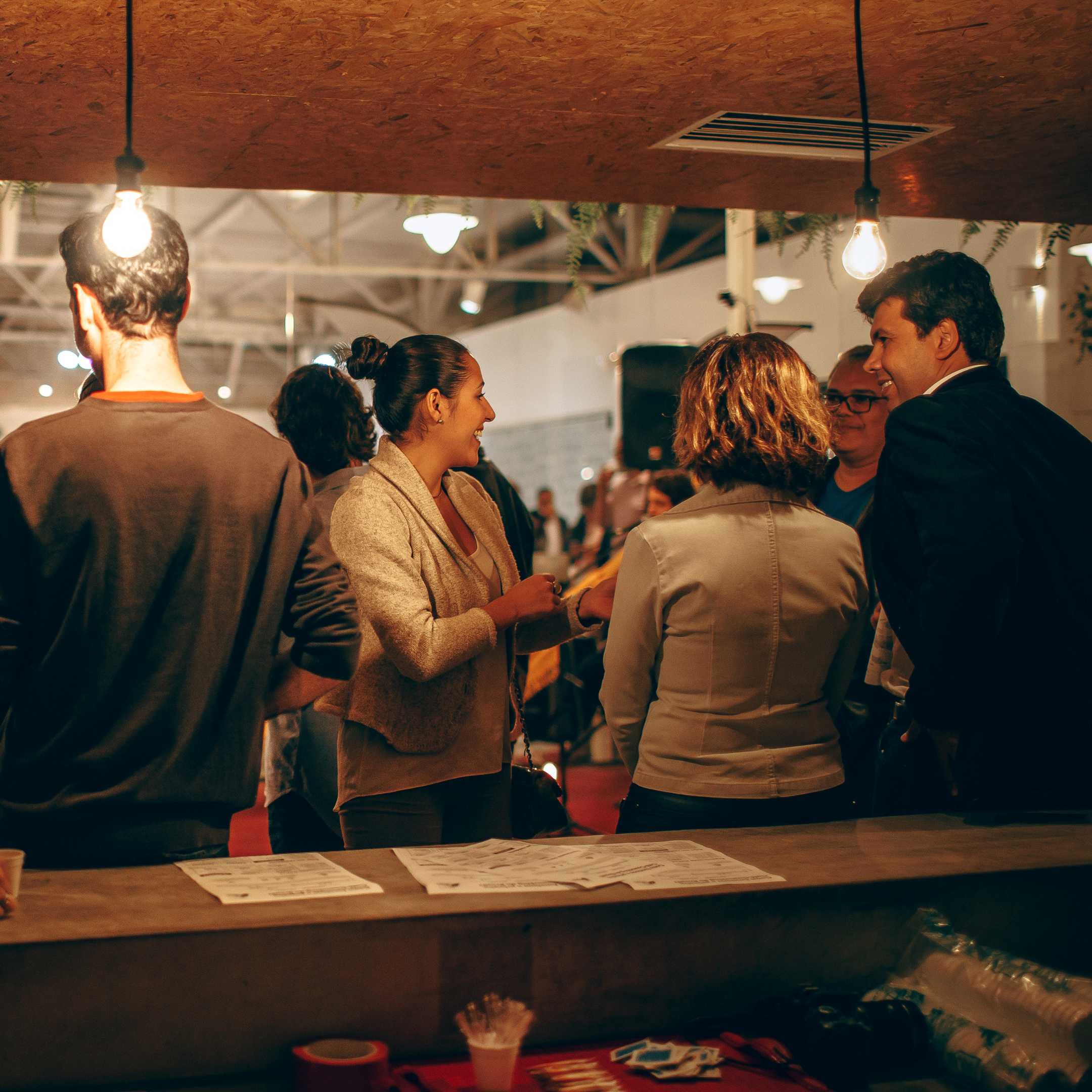 Personas en una reunión social, conversando y sonriendo en un ambiente con iluminación cálida y decoraciones modernas.