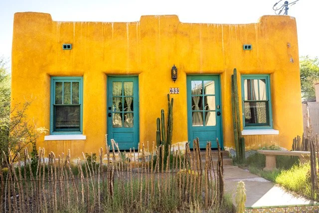 Bright yellow-orange house with green shutters and cacti out front