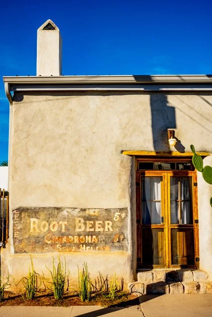 Building with tan wooden doors bearing a faded sign that says root beer 5 cents