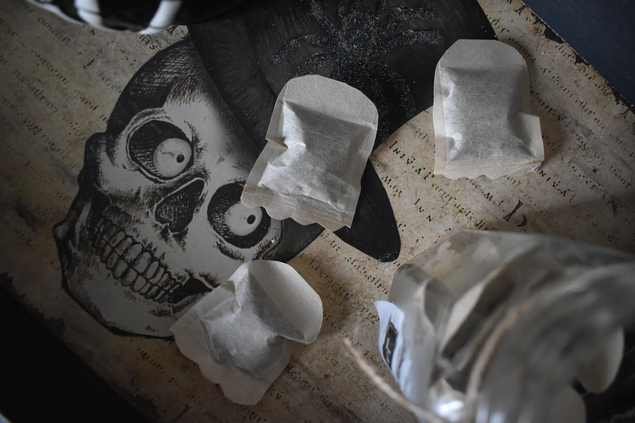 tea bags cut into ghost shapes spread out on a tray with a skull design