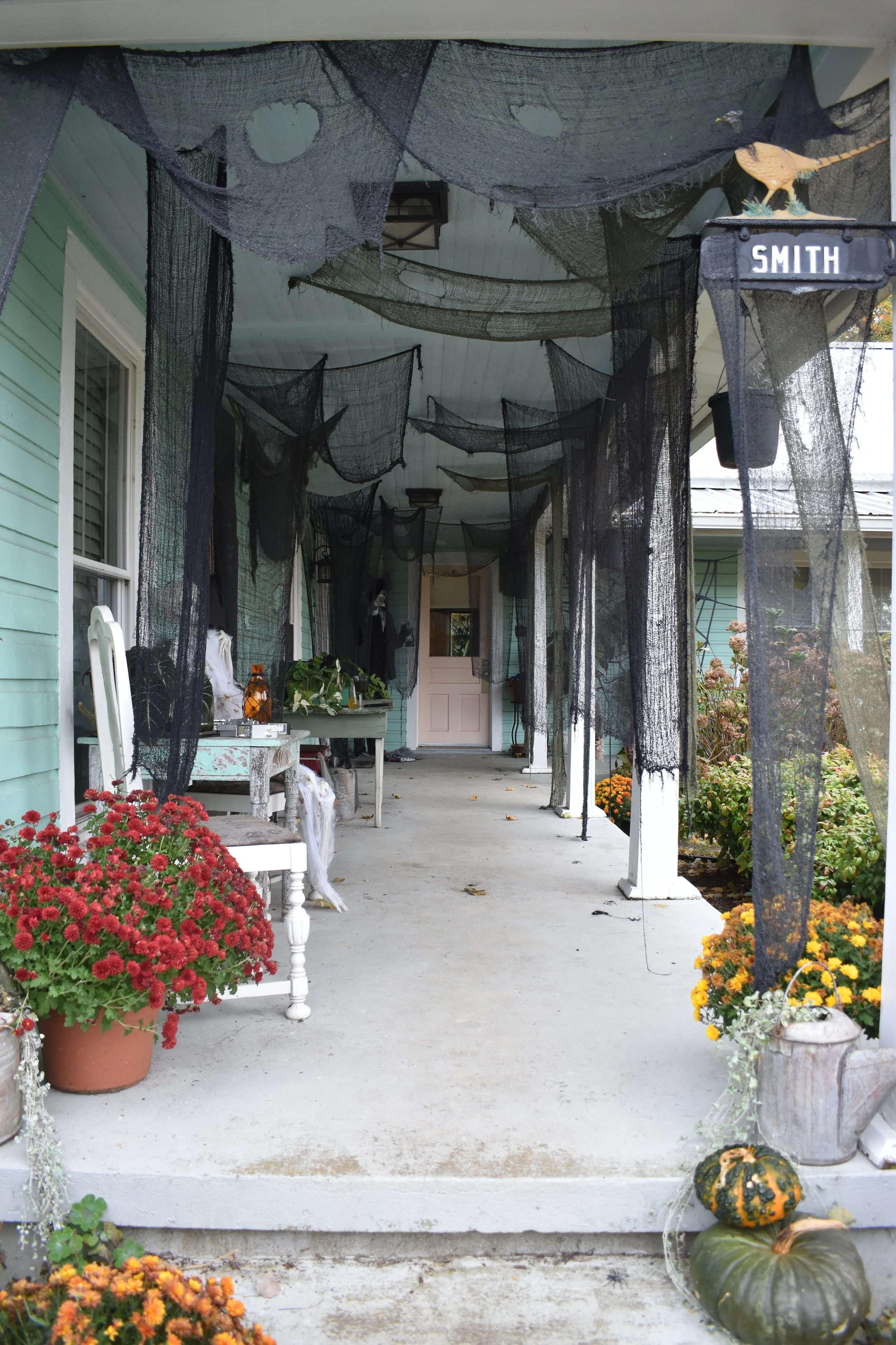 front porch with fall flowers and creepy cloth hanging from the ceiling