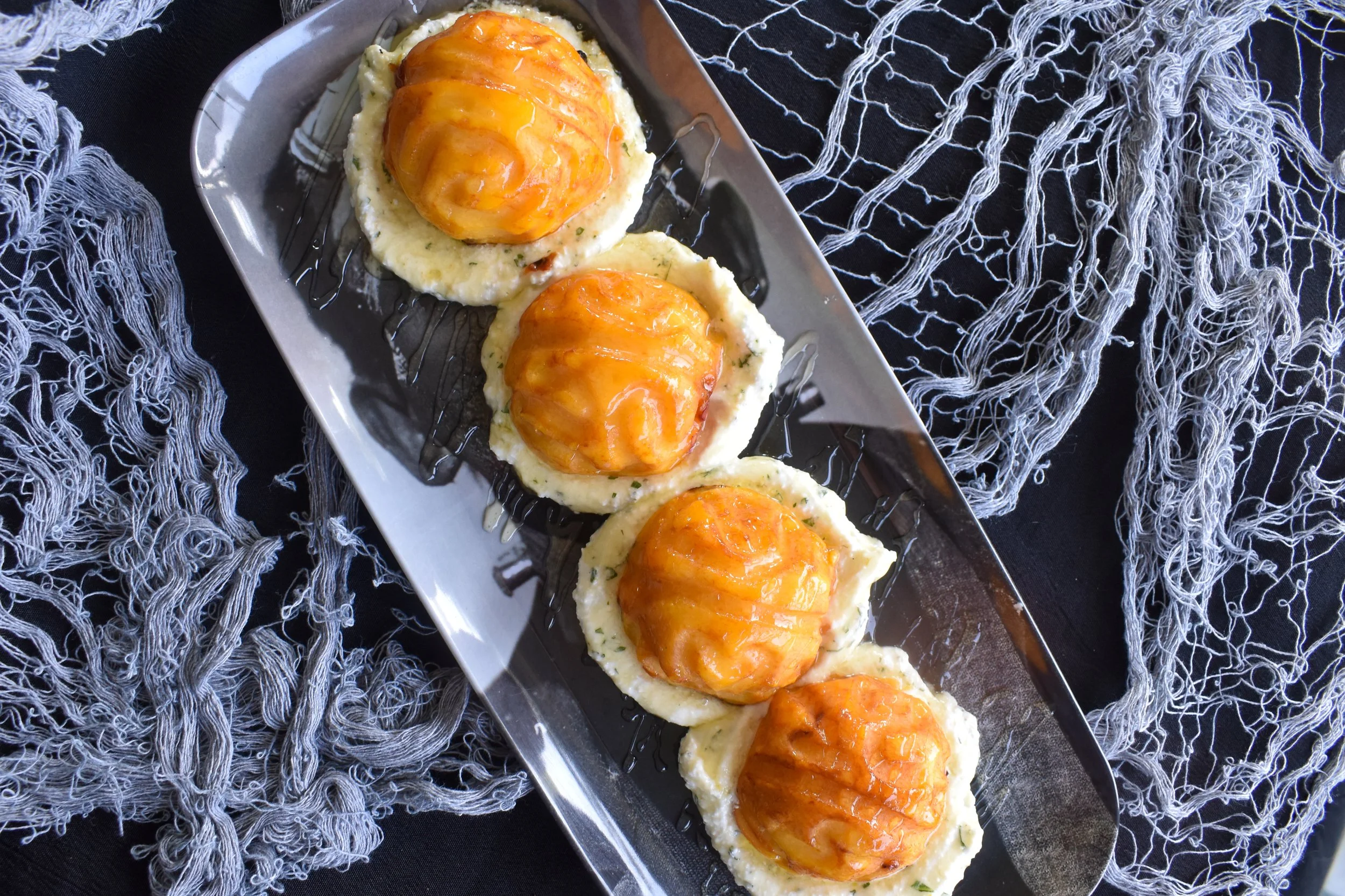 Overhead image of grilled peaches carved to look like brains on a bed of ricotta sitting on a Frankenstein tray