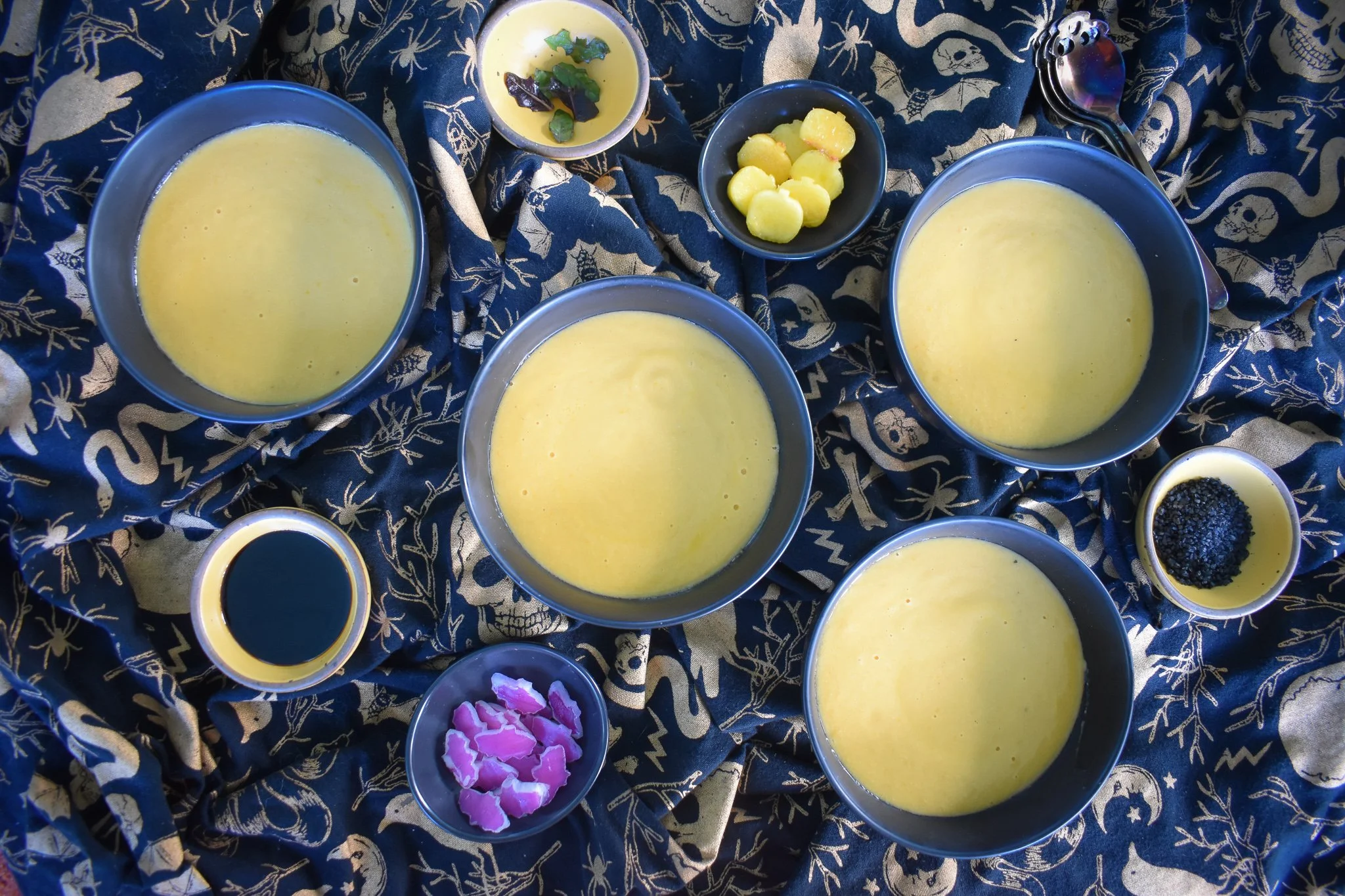 bowls of gazpacho and garnishes on a black ang gold Halloween tablecloth