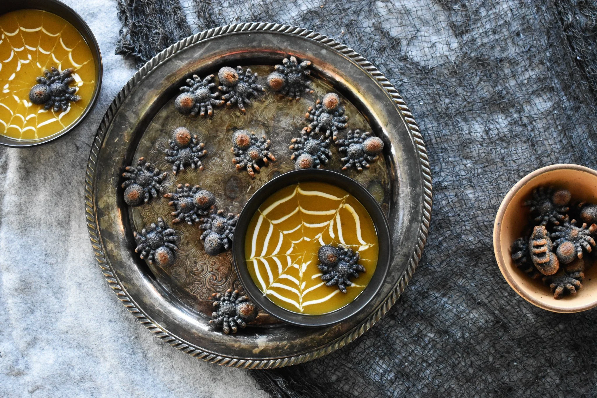 Bowl of soup on a silver platter surrounded by spiders made of blue cornbread