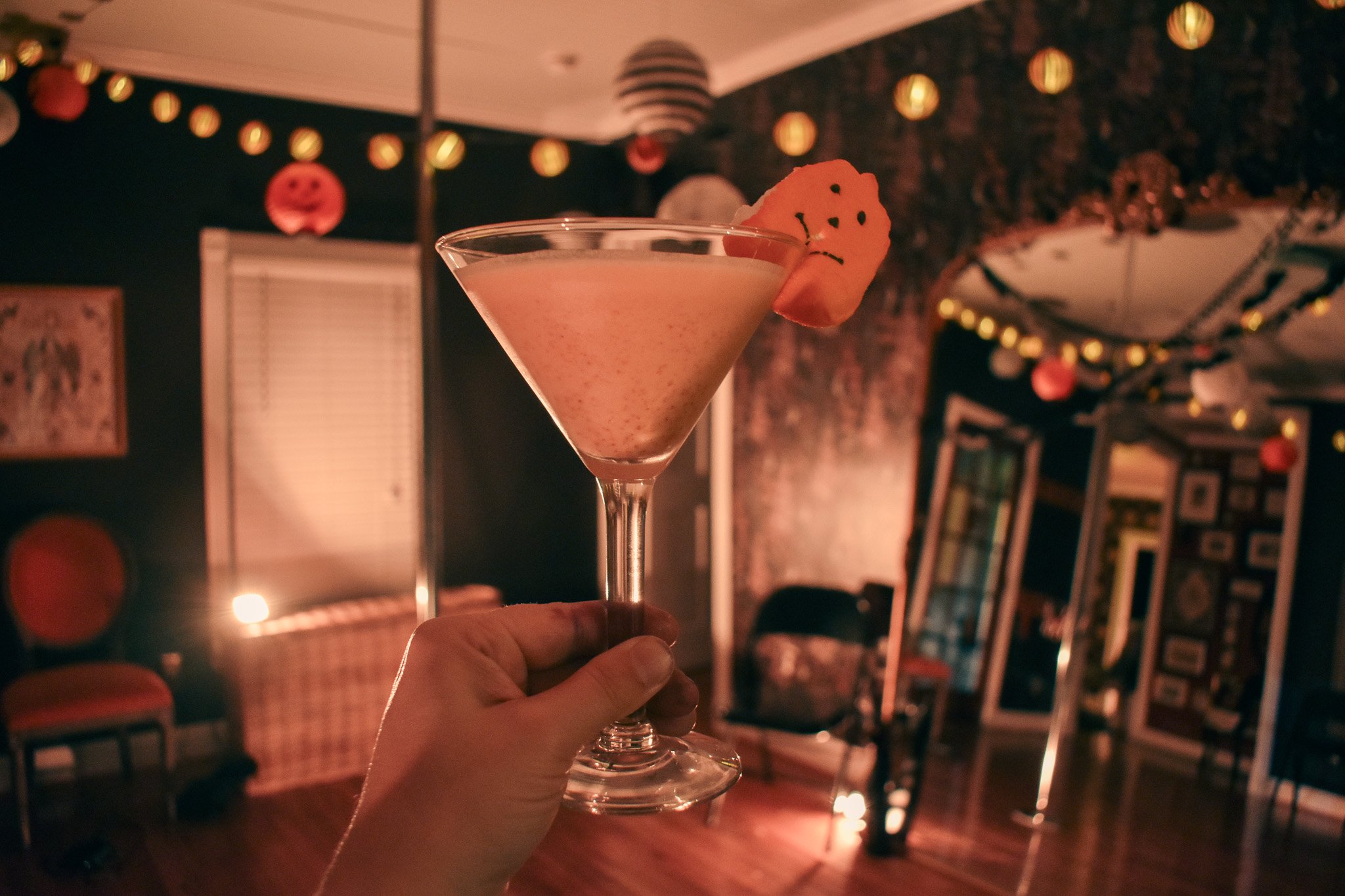a hand holding up a martini glass with a marshmallow pumpkin on the side