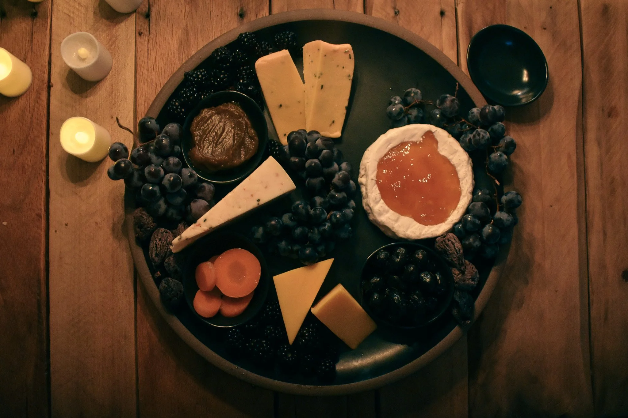 cheese wedges. tiny bowls, and fruits on a black platter