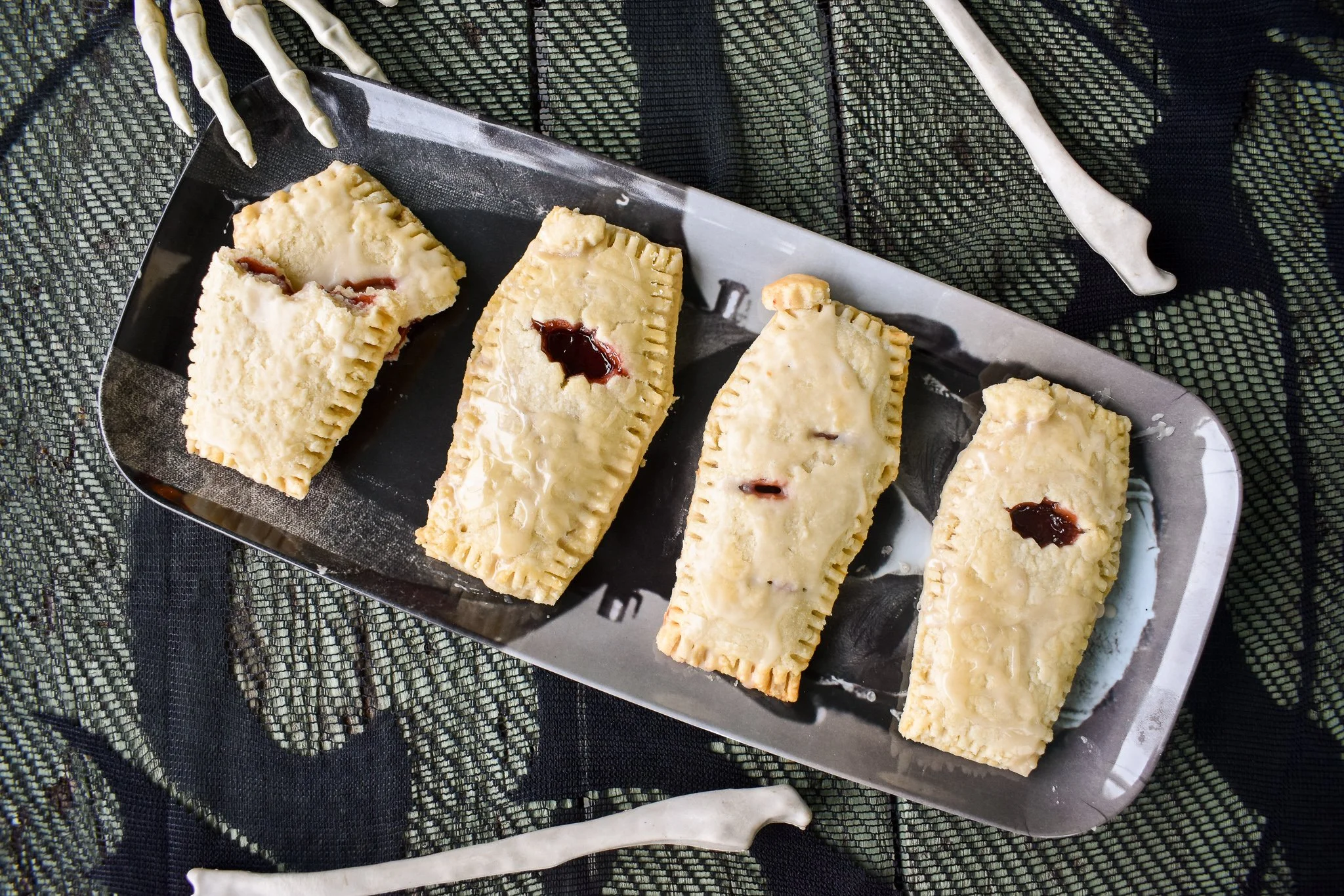 coffin shaped pastries on a tray with a skeletal hand reaching for them