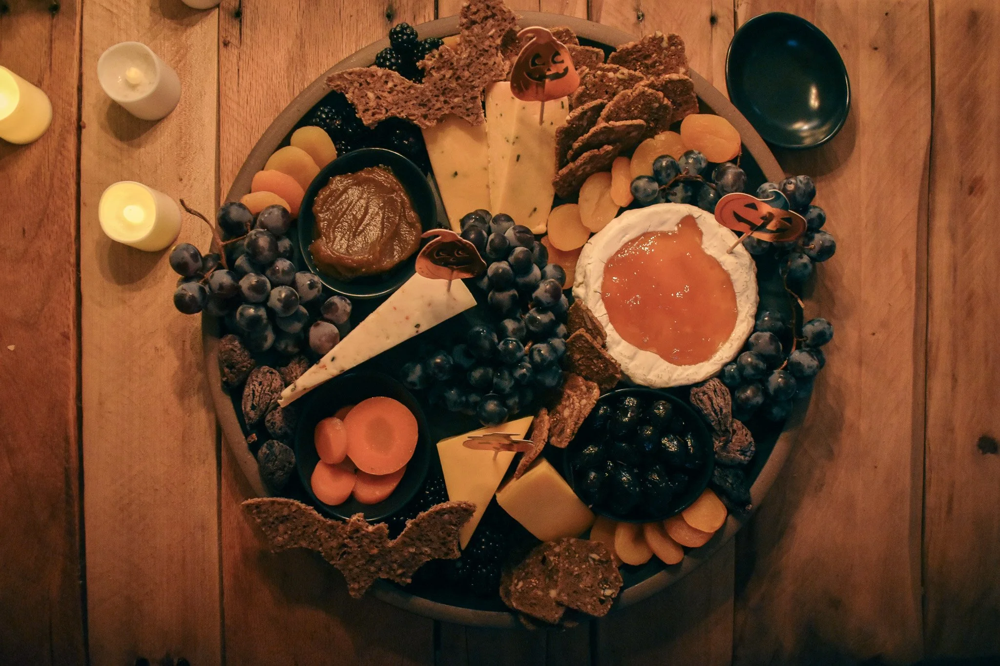 cheese wedges. tiny bowls, fresh fruits, dried fruits, crackers, and bat shaped bread  on a black platter