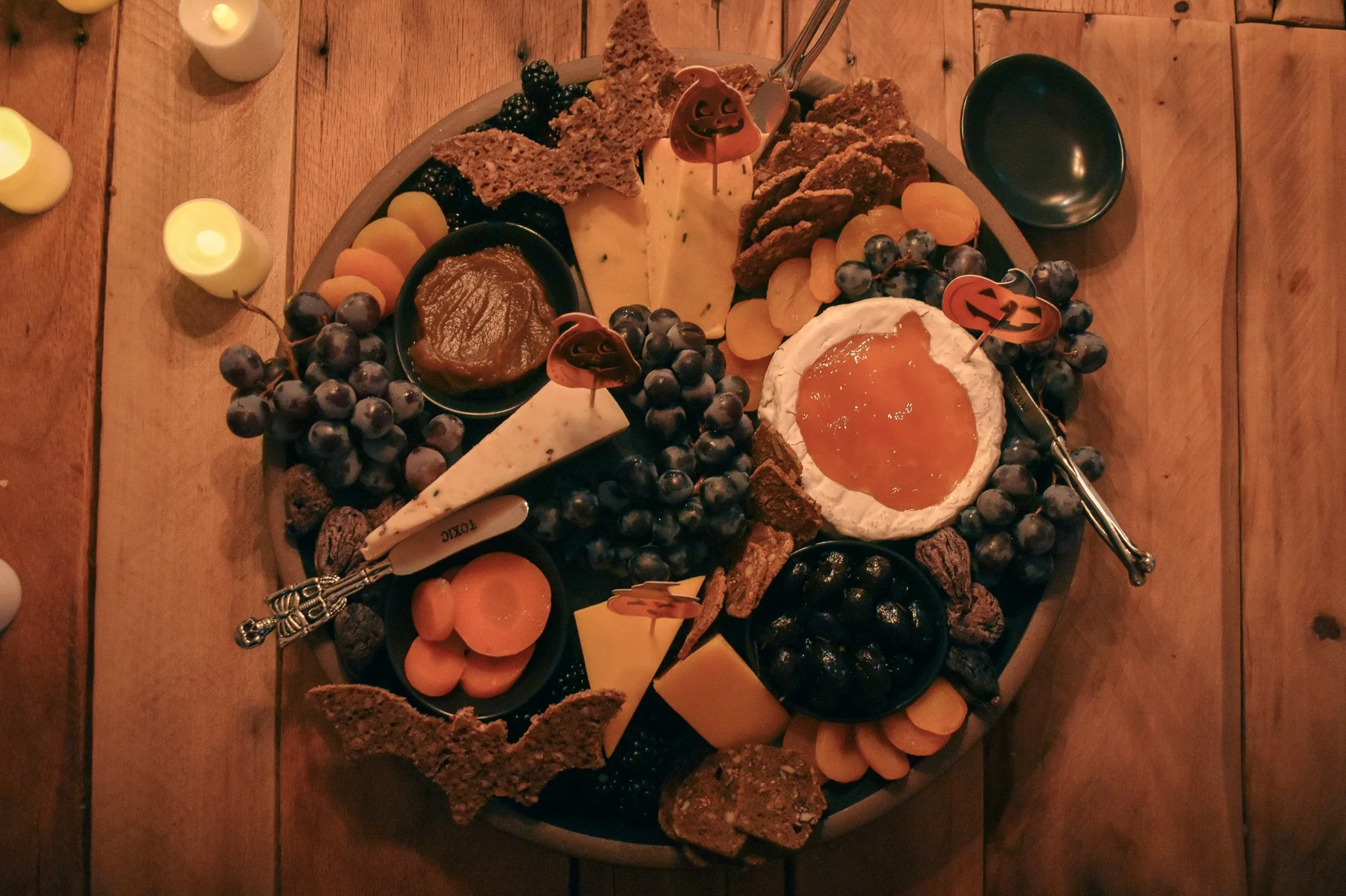 cheese wedges. tiny bowls, fresh fruits, dried fruits, crackers, bat shaped bread, and bone serving utensils  on a black platter