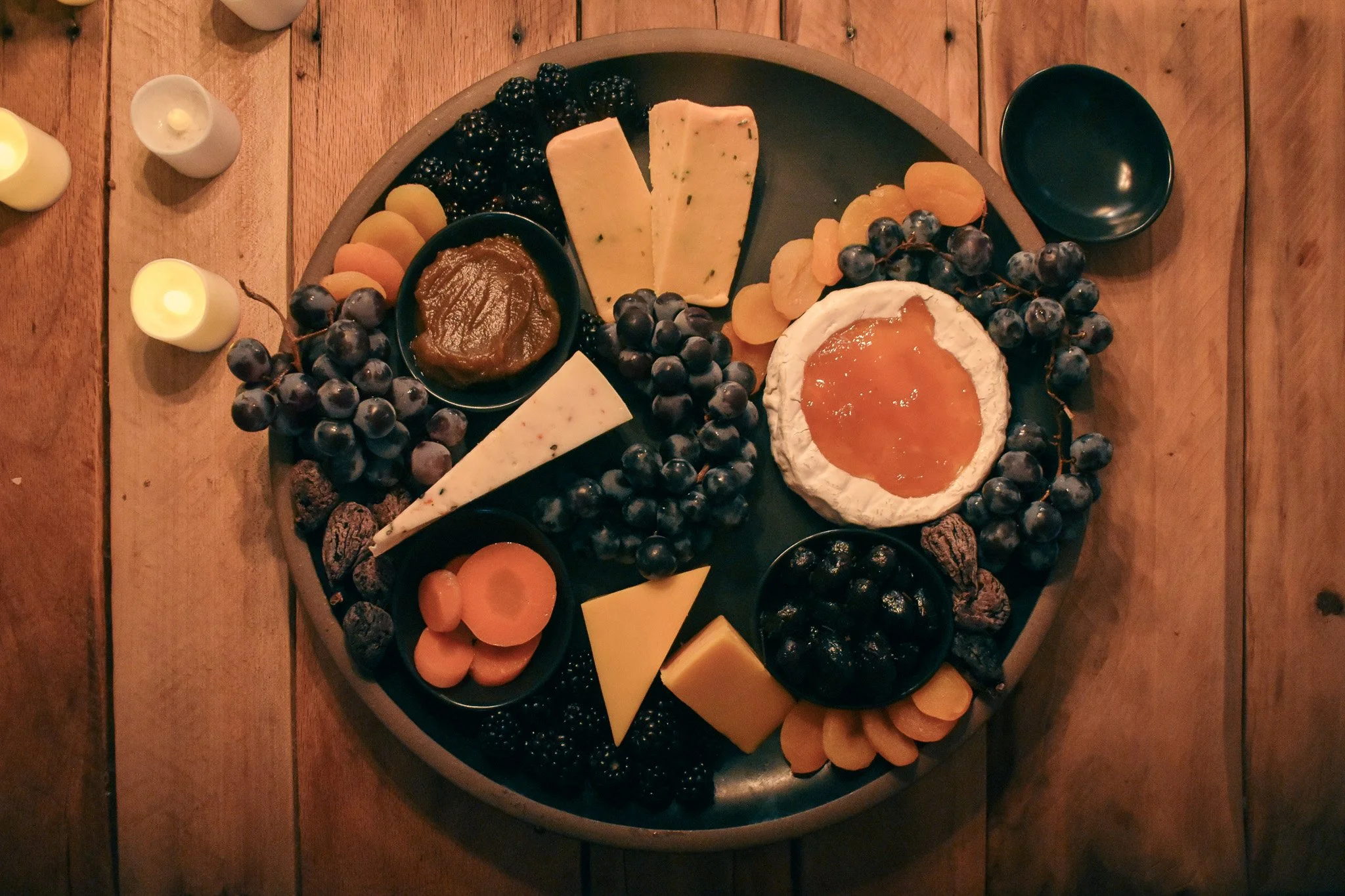 cheese wedges. tiny bowls, fresh fruits, and dried fruits on a black platter