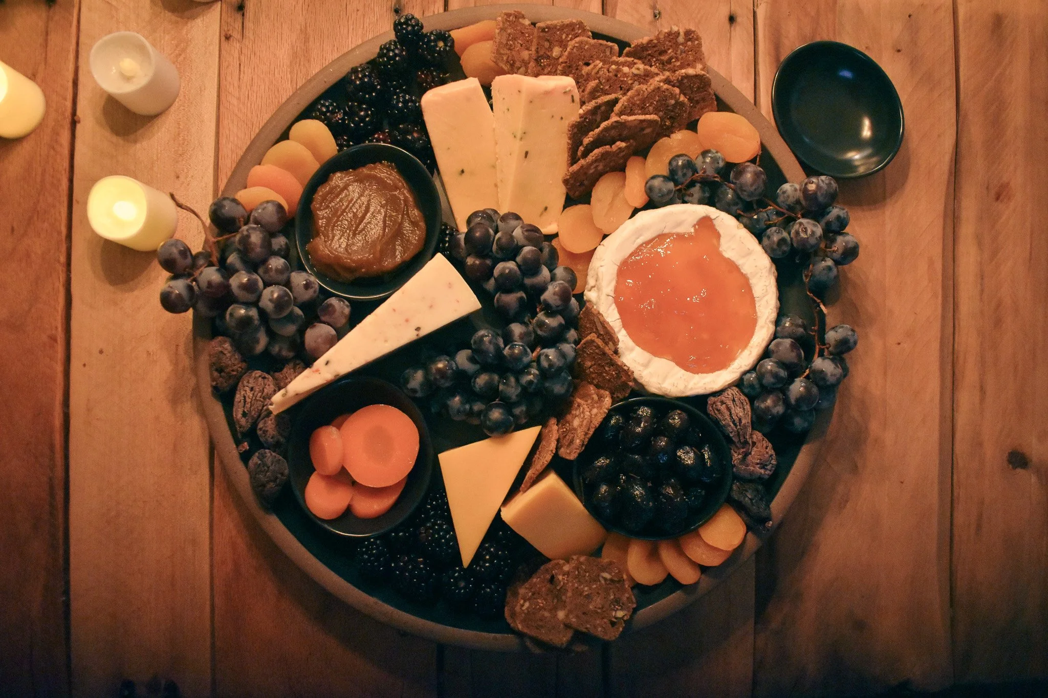 cheese wedges. tiny bowls, fresh fruits, dried fruits, and crackers on a black platter