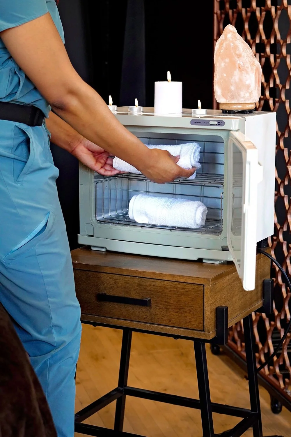 Massage therapist placing towels into a towel warmer.