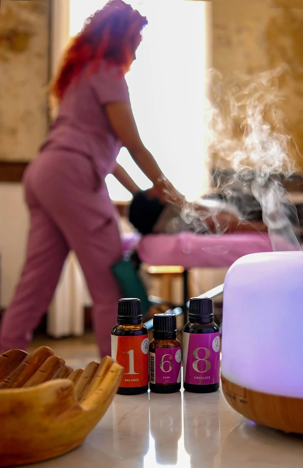Aromatherapy diffuser and essential oils with a relaxing massage taking place in the background.