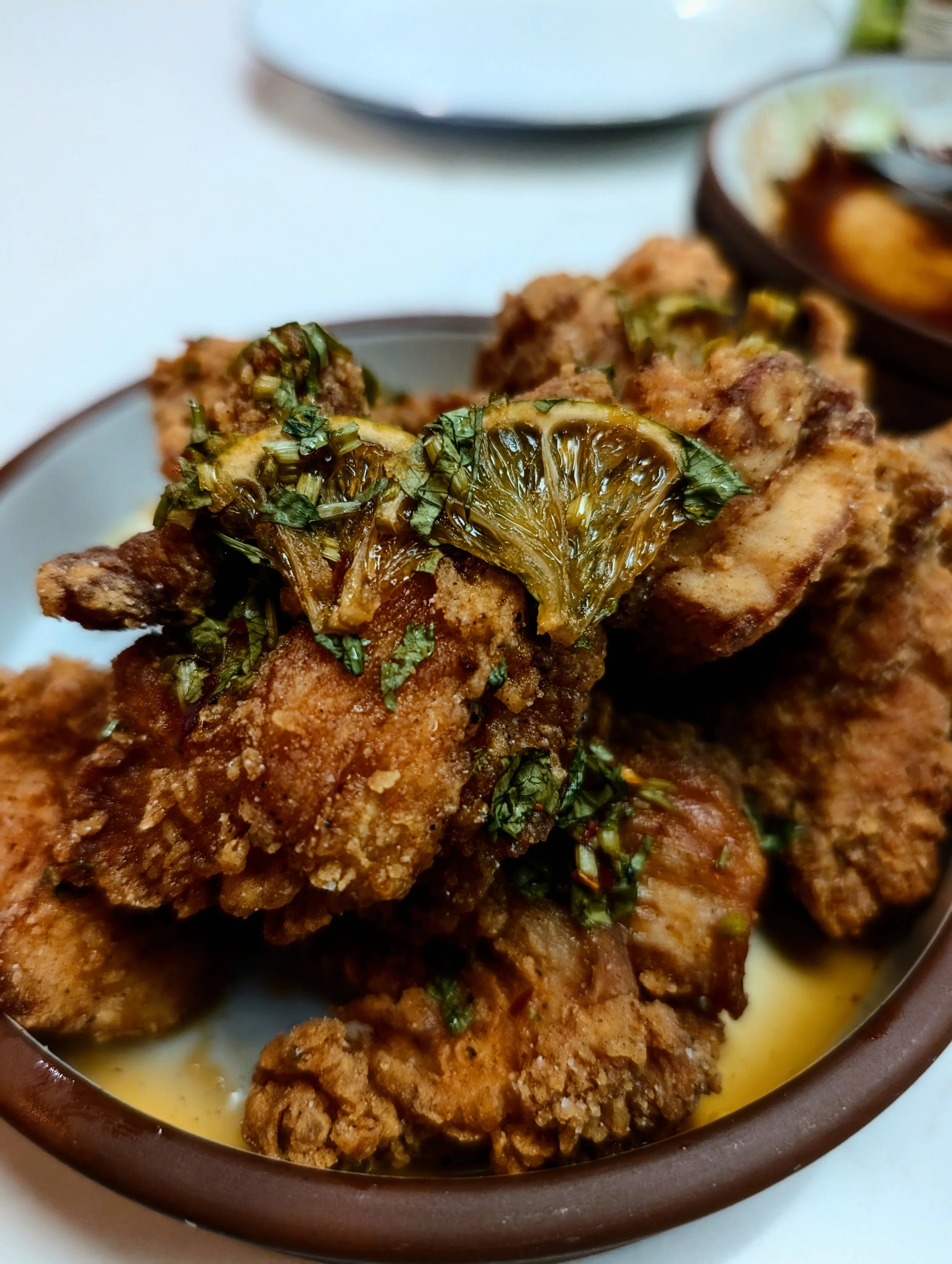 Fried chicken pieces garnished with chopped herbs and lemon slices, served in a brown dish