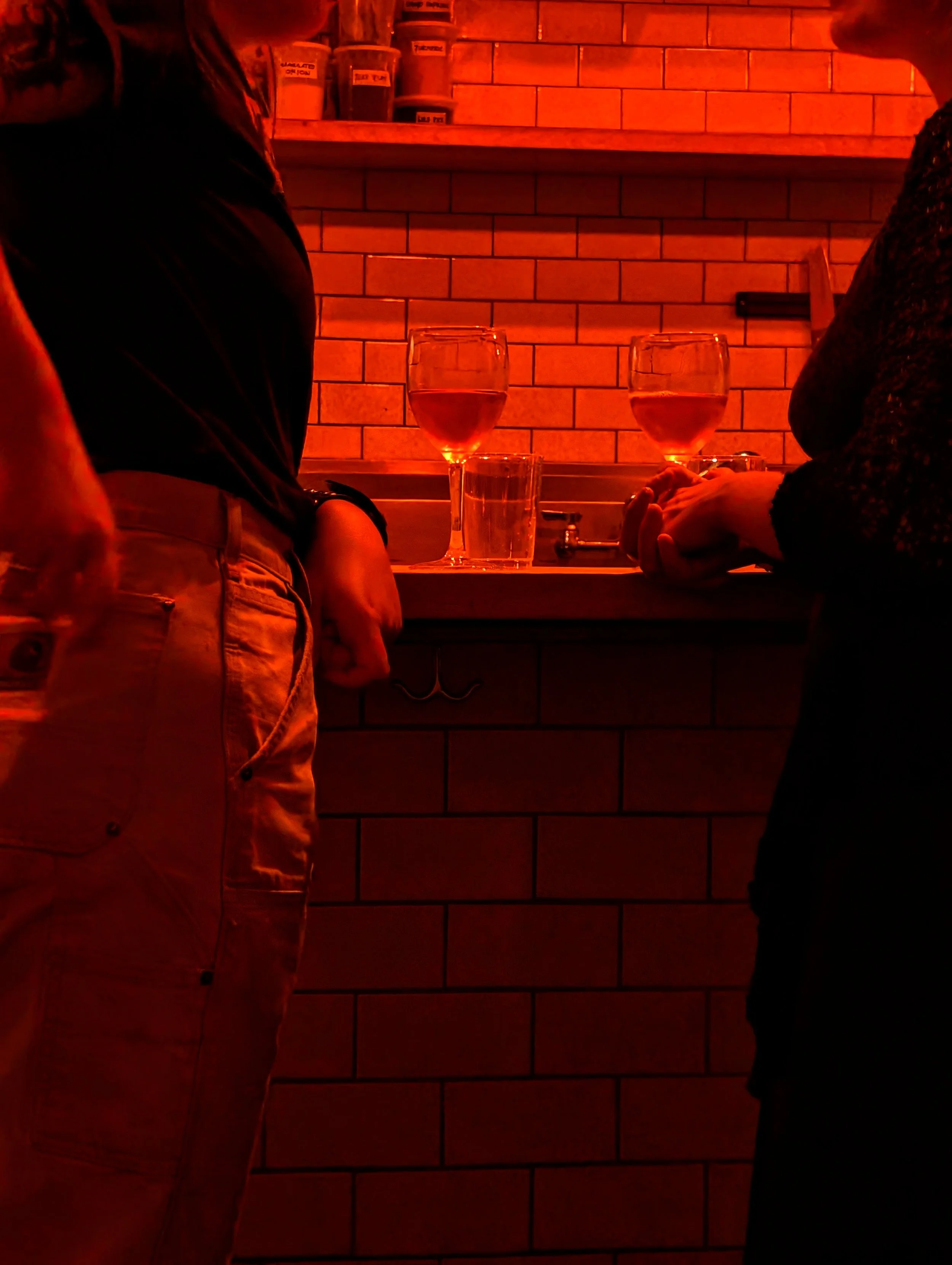 Two people talking in a dimly lit bar with glasses of wine and water on the counter.