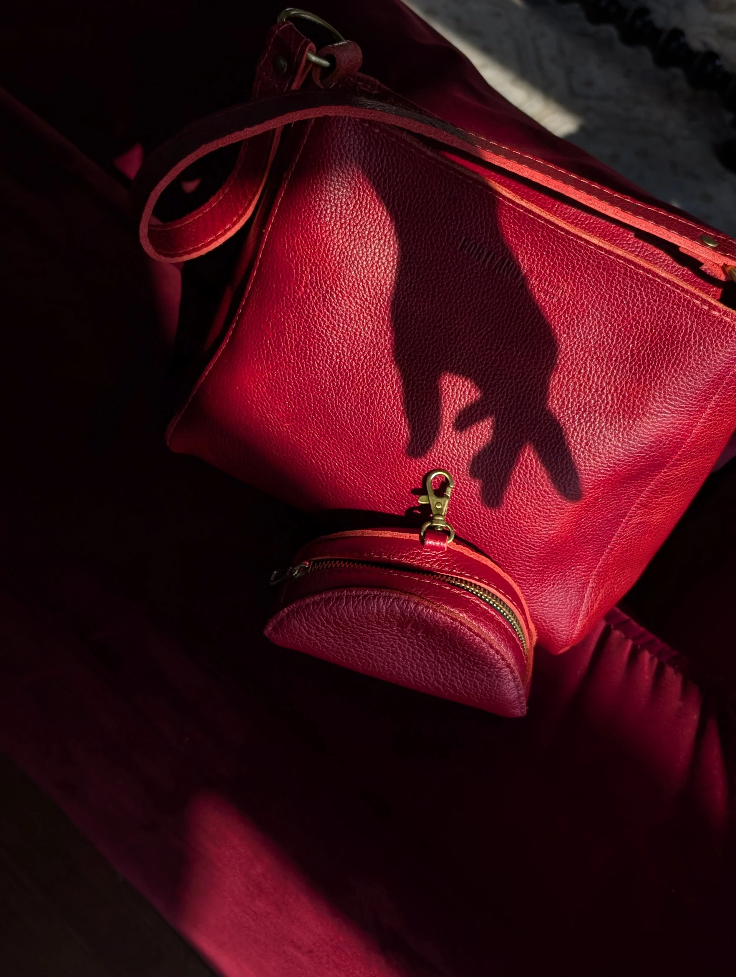 Red handbag with a shadow cast of a hand reaching towards it, placed on a dark red surface.