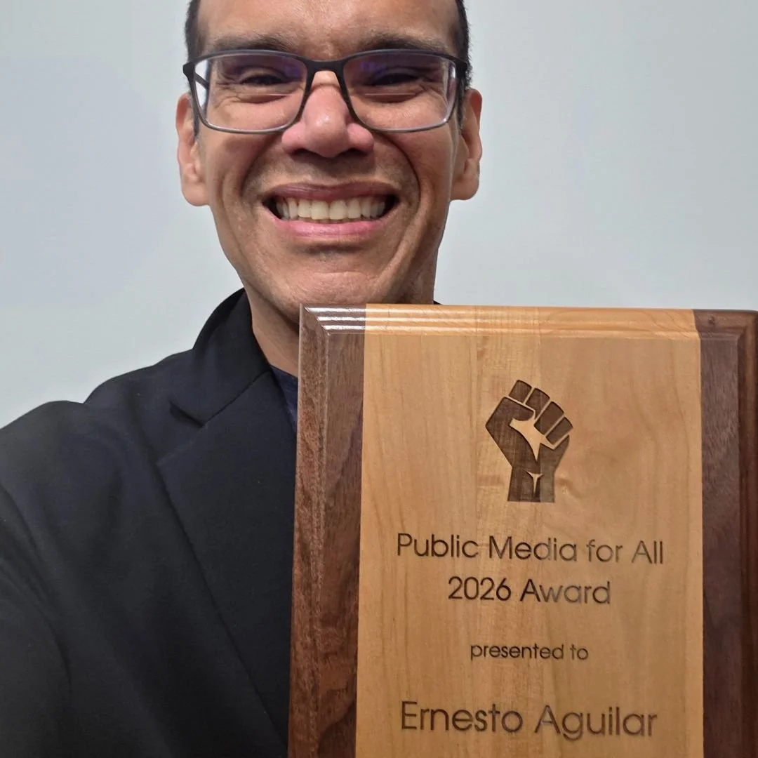 Ernesto Aguilar wearing a black suit coat and holding the PMFA Award plaque