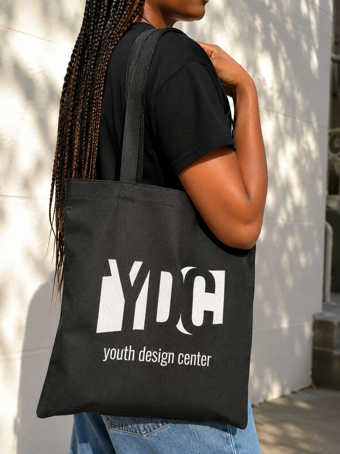 Black tote bag featuring the white Youth Design Center logo on the front